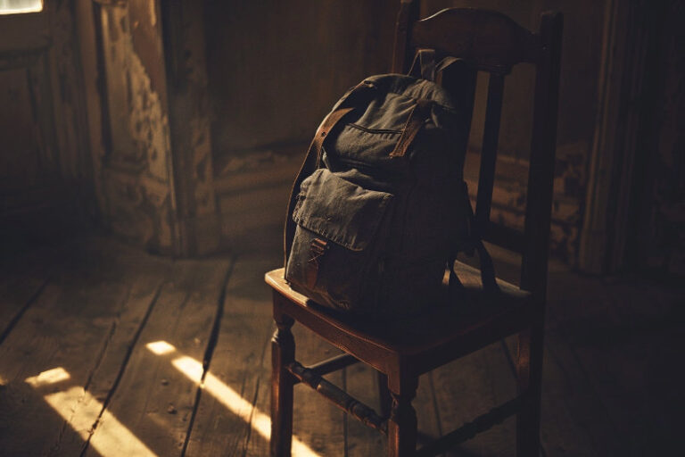 plecak spoczywający na krześle w półmroku, symbol ciężaru i odpoczynku po długiej drodze