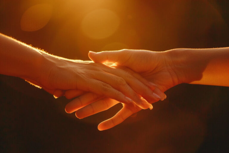 dłonie dotykające się delikatnie w ciepłym świetle – symbol bliskości, zaufania i dotyku, który leczy